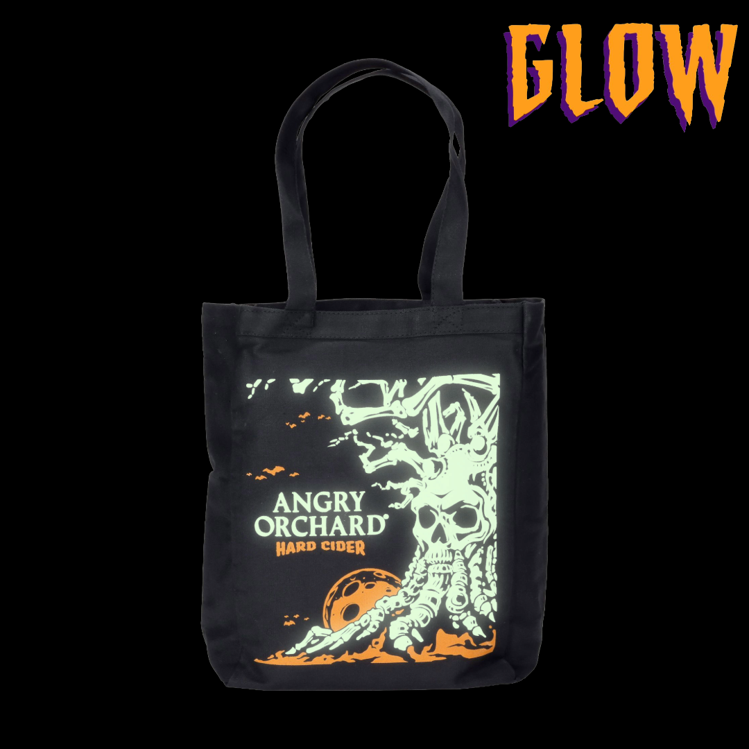 Black tote bag with Angry Orchard Hard Cider design featuring a skull inspired tree design. GLOW text describing glow in the dark feature of the skeleton tree.