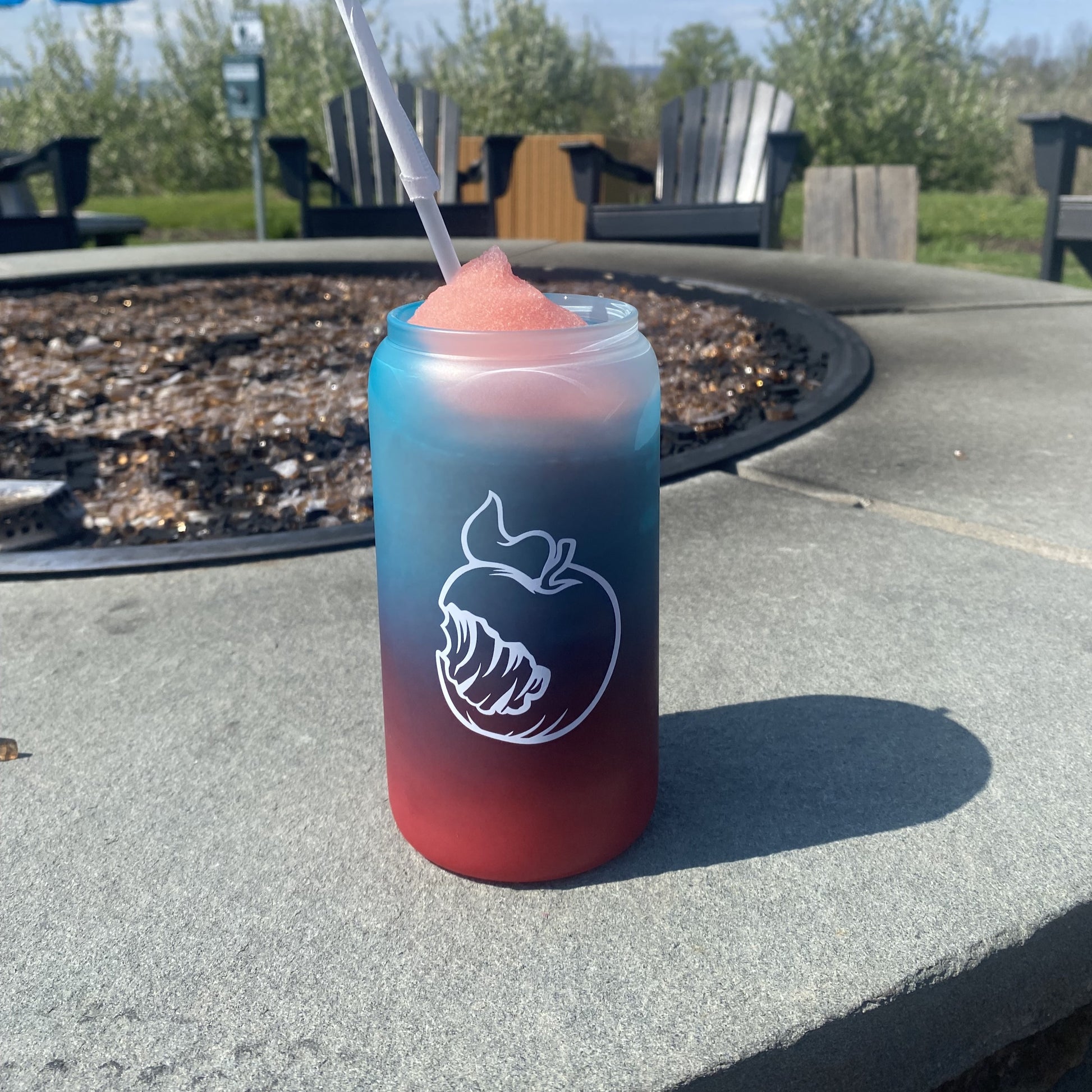 A frosted 16oz can-shaped glass with a pink-to-mint ombre gradient. One side shows the Angry Orchard logo with "Walden, New York" text; the other side features the brand's signature bitten apple icon. In a third image, the glass is filled with a frozen drink, revealing a bright red-to-blue ombre color change.